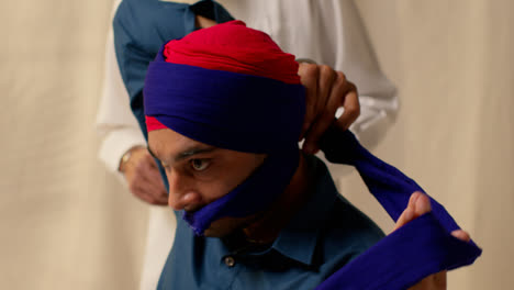 Close-Up-Studio-Shot-Of-Two-Sikh-Men-Tying-Fabric-For-Turban-Against-Plain-Background